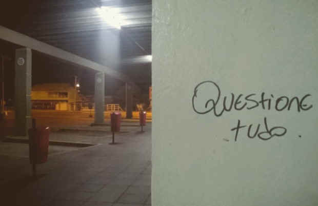 A bus station pillar that reads "Question everything" written in black marker pen.